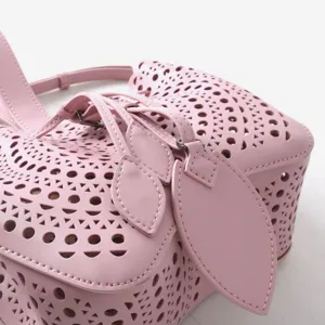 Détail de sac seau ajouré en cuir rose avec motifs géométriques et pendentifs feuilles.