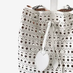 Sac seau en cuir blanc avec motif ajouré géométrique, lien de serrage et breloques élégantes.