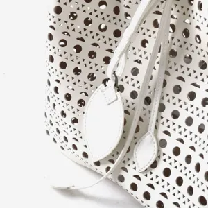 Detail de sac seau en cuir blanc avec motif perfore geometrique et pendentif feuille sus.