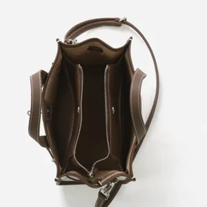 Vue de detail superieure du cabas marron en cuir et toile avec compartiments et fermeture.