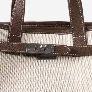 Détail d'un sac cabas en toile et cuir avec poignées robustes et fermoir métallique.