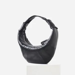 Detalle del bolso croissant negro de cuero suave con textura de piel de oveja y diseño plisado.