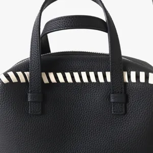 Gros plan détail du sac à main boston en cuir véritable noir avec coutures tissées blanches.
