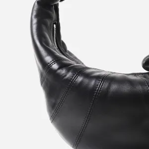 Detalle de bolso croissant de piel negra, suave textura de cordón, cierre curvo, costuras finas