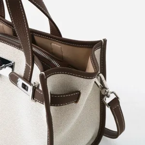 Détail du sac cabas en toile et cuir avec bordure marron et accessoires en argent.