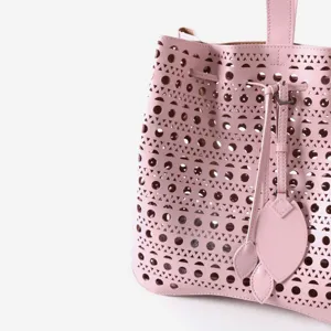 Gros plan sur les details du sac seau en cuir rose avec motif ajoure geometrique et liens.