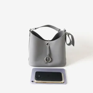 Sac seau en cuir véritable gris avec fermeture à anneau métallique et poignée supérieure.