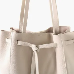 Gros plan detail du sac cabas en cuir veritable beige avec fermeture a cordon et lanieres.
