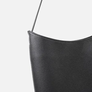 Dettaglio in primo piano di una borsa a spalla in vera pelle nera dal design minimalista.