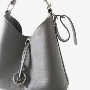 Gros plan détaillé du sac seau en cuir gris avec élégants accessoires et anneaux en métal.