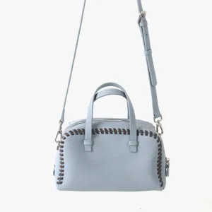Gros plan detail du sac a main boston en cuir bleu clair avec bordure surpiquee marron et sangle.
