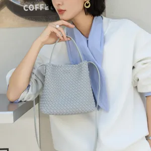 Gros-plan du sac seau en cuir tressé gris clair, avec sangle fine et poignée élégante.