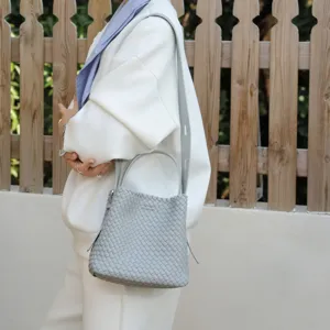 Vue de détail du sac seau en cuir tressé gris avec poignée et bandoulière dans une scène de vie.