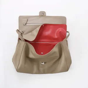Vue détaillée du sac en cuir taupe avec doublure intérieure rouge et pièces métalliques.