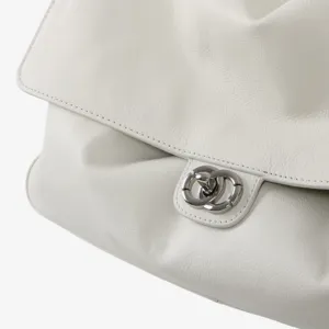Détail de sac à main en cuir blanc montrant une texture souple, un rabat et un fermoir argenté.