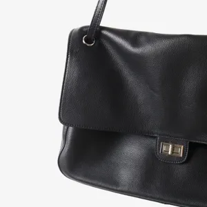 Sac à bandoulière en cuir noir détail gros plan avec fermoir tournant et texture douce.