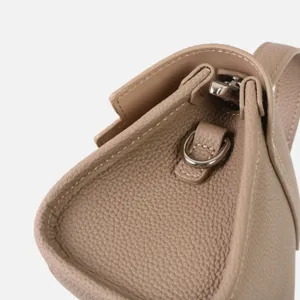 Gros plan sur les détails du sac bandoulière en cuir taupe avec quincaillerie métal.
