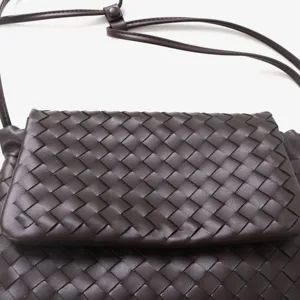 Détail de sac bandoulière à rabat en cuir tissé marron foncé, texture premium, style chic.