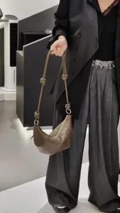 Détail de sac bandoulière croissant en cuir marron avec lanière nouée et anneau métal.