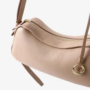 Gros plan détaillé d'un sac cylindrique en cuir grainé avec fermeture éclair dorée et anneau.