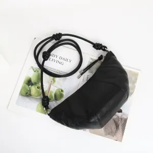 Vue détaillée du sac porté épaule croissant en cuir noir posé sur un magazine de mode.