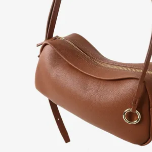 Gros plan détail du sac cylindre en cuir marron naturel avec fermeture éclair dorée.