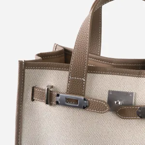 Détail de sac cabas en toile et cuir avec coutures soignées et ferrures métalliques.