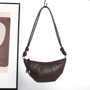 Détail de sac bandoulière croissant en cuir marron foncé, lanière nouée et design.