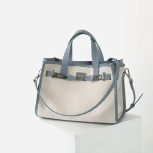 Détail de sac cabas en toile et cuir avec fermeture à serrure métallique et double poignée.