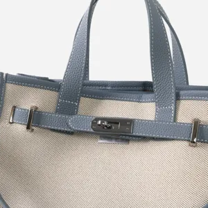 Détail de sac cabas en toile et cuir, avec fermoir métallique raffiné et lanière contrastée.