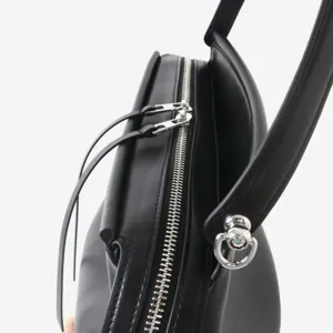 Détail de sac à bandoulière en cuir noir montrant une fermeture éclair et quincaillerie.