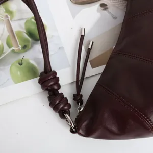 Vue détaillée de la lanière en cuir bordeaux du sac et des pièces métalliques.
