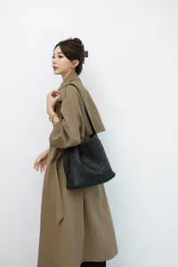 Vue de détail élégante du sac cabas en cuir tressé noir porté par le mannequin en trench.