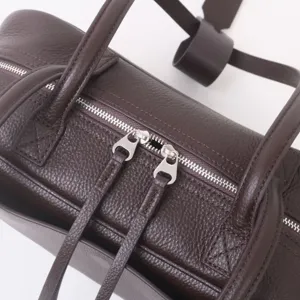 Detalle de bolso bowling de piel marron oscuro con textura premium y cremalleras metalicas.