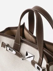 Sac cabas en toile et cuir veritable avec fermeture metallique et poignees elegantes.