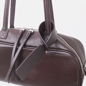 Vista detallada del bolso tipo bolos de cuero marrón oscuro con textura prémium y asas dobles.