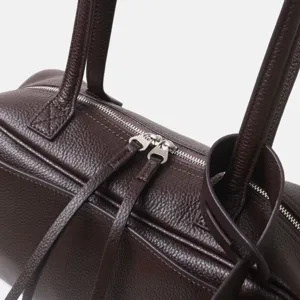 Detalle del bolso de cuero marrón oscuro con textura de alta calidad y cremallera metálica.