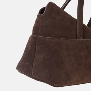 Vue détaillée de sac à main en daim marron montrant la finition en cuir et les coutures.