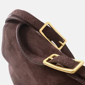 Détail de sac bandoulière en cuir suédé marron, boucle dorée élégante, texture.