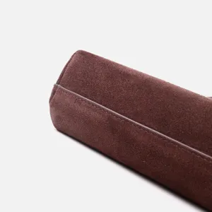 Détail de sac à main en cuir suédé marron foncé, texture givrée, design élégant et courbé.