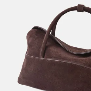 Détail de sac à main en daim marron, finition artisanale et texture douce de cabas minimaliste.