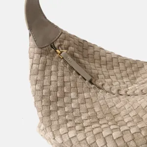 Gros plan détail de la texture du sac hobo en cuir tissé luxueux avec fermeture éclair dorée.