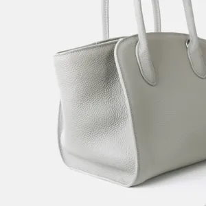 Détail d'un sac cabas minimaliste en cuir gris, doté d'une texture grainée et de doubles poignées.