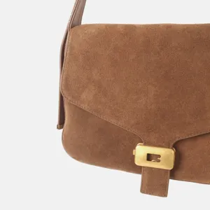 Gros plan d'un sac bandoulière en daim marron avec un détail de verrou en métal doré.