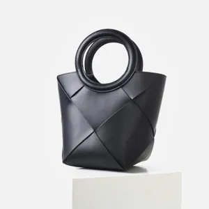Detail view of black woven leather handbag, featuring geometric macro weave and round handles.