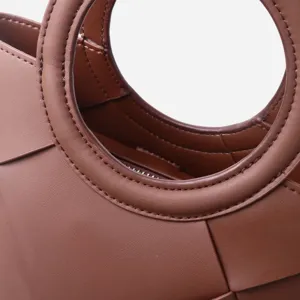 Brown woven leather handbag detail featuring a stylish circular handle and premium texture.