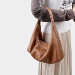 Gros plan d'un sac porté épaule souple en cuir marron, montrant la fermeture et texture.