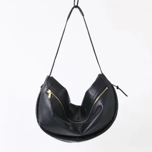 Détail de sac bandoulière croissant en cuir noir avec fermeture à glissière métallique incurvée.