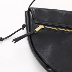 Gros plan détail du sac bandoulière demi-lune en cuir noir avec fermeture éclair dorée.