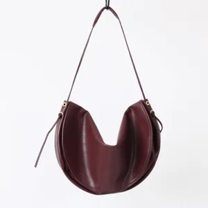 Gros plan d'un sac porté épaule croissant en cuir rouge foncé au design élégant.
